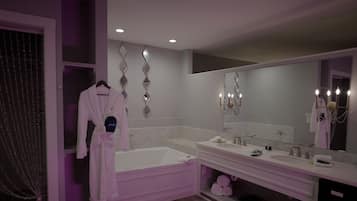 Une salle de bain moderne avec une baignoire, deux lavabos, un grand miroir et des appliques murales décoratives.