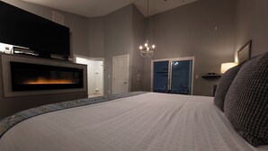 A hotel room with a large bed, a flat-screen TV mounted on the wall, a fireplace, a chandelier, and a wardrobe. - Belamere Swimming Pool Suites (Cumming)