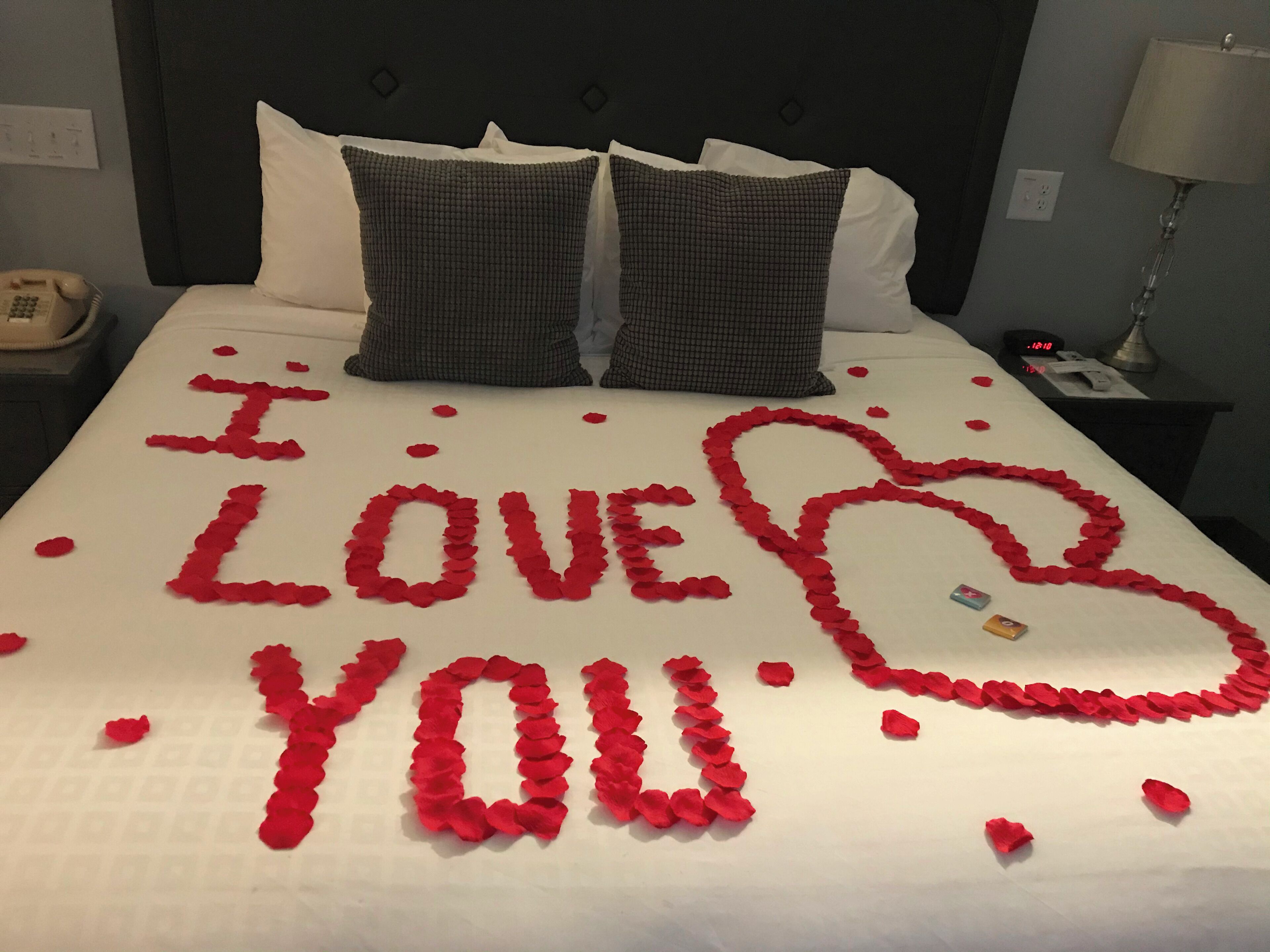 A bed with rose petals arranged to spell "I LOVE YOU" and a heart shape.