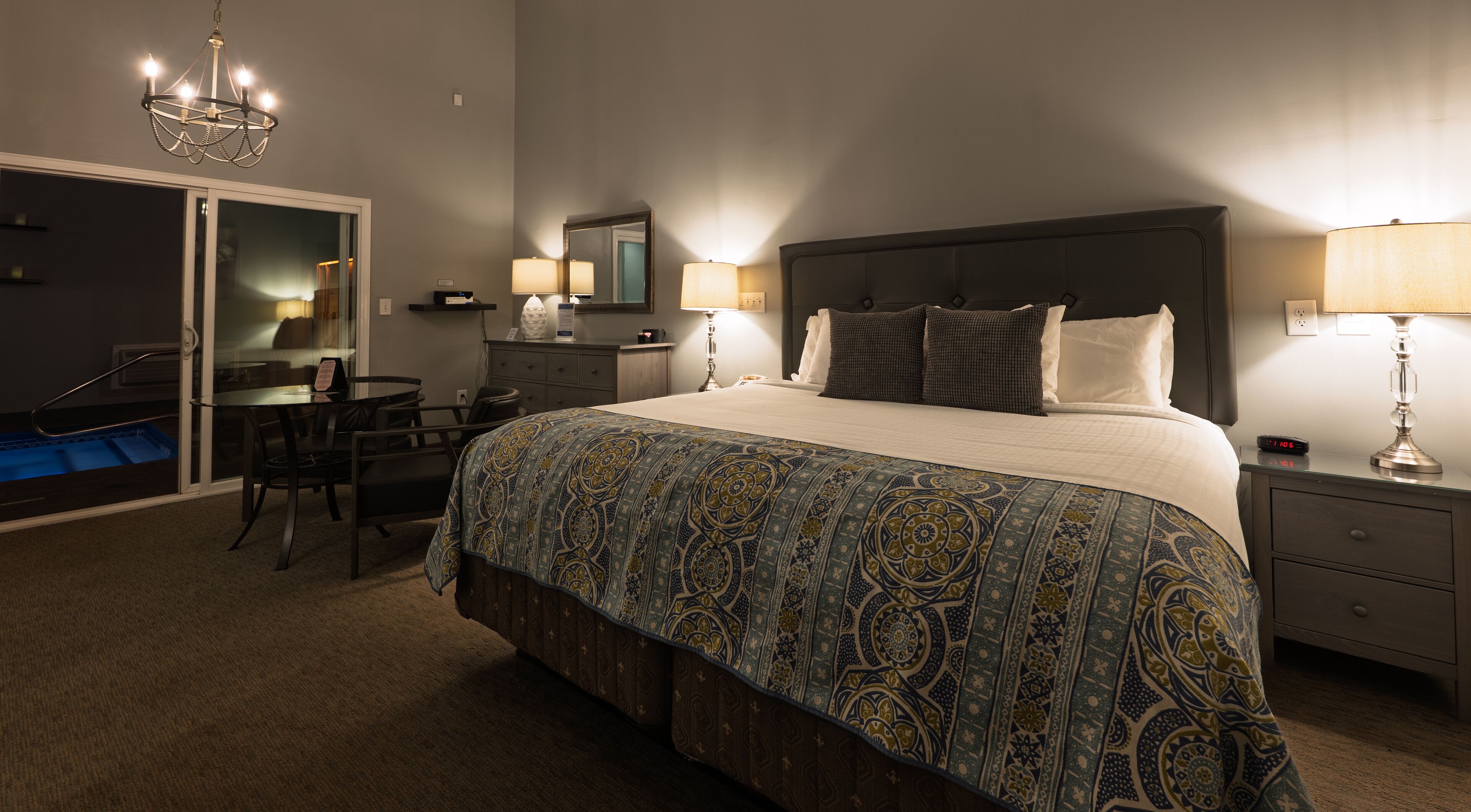 Quarto de hotel com uma cama grande, duas mesas de cabeceira com luminárias, uma escrivaninha com cadeira, um armário e um lustre.