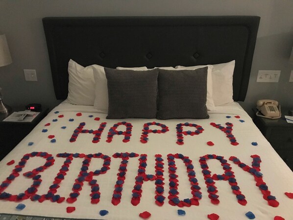 A hotel room with a bed, pillows, a nightstand with a phone, and a wall clock.