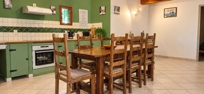 Uma sala de jantar com mesa e cadeiras de madeira, cozinha verde com azulejos brancos e forno branco.