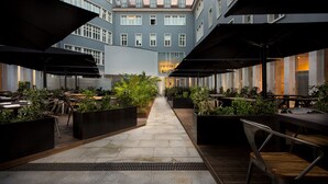 An outdoor dining area with tables and chairs, surrounded by planters and umbrellas, leading to a building with large windows. - Lisbon Finestay 8 Building (Lisbon)