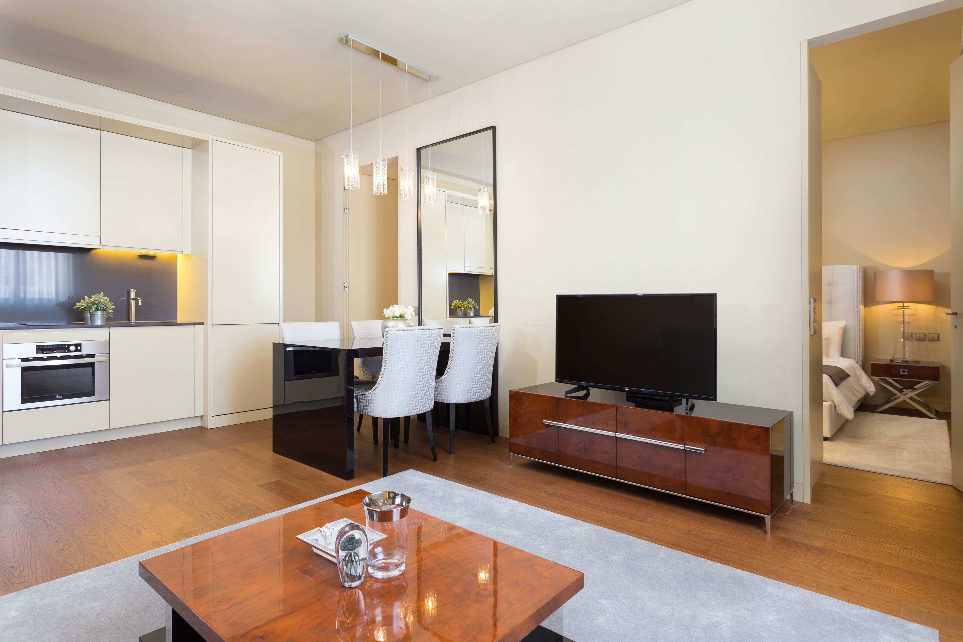 Ein modernes Wohnzimmer mit Flachbildfernseher, Essbereich mit Stühlen, Couchtisch und einer Küche mit Backofen.