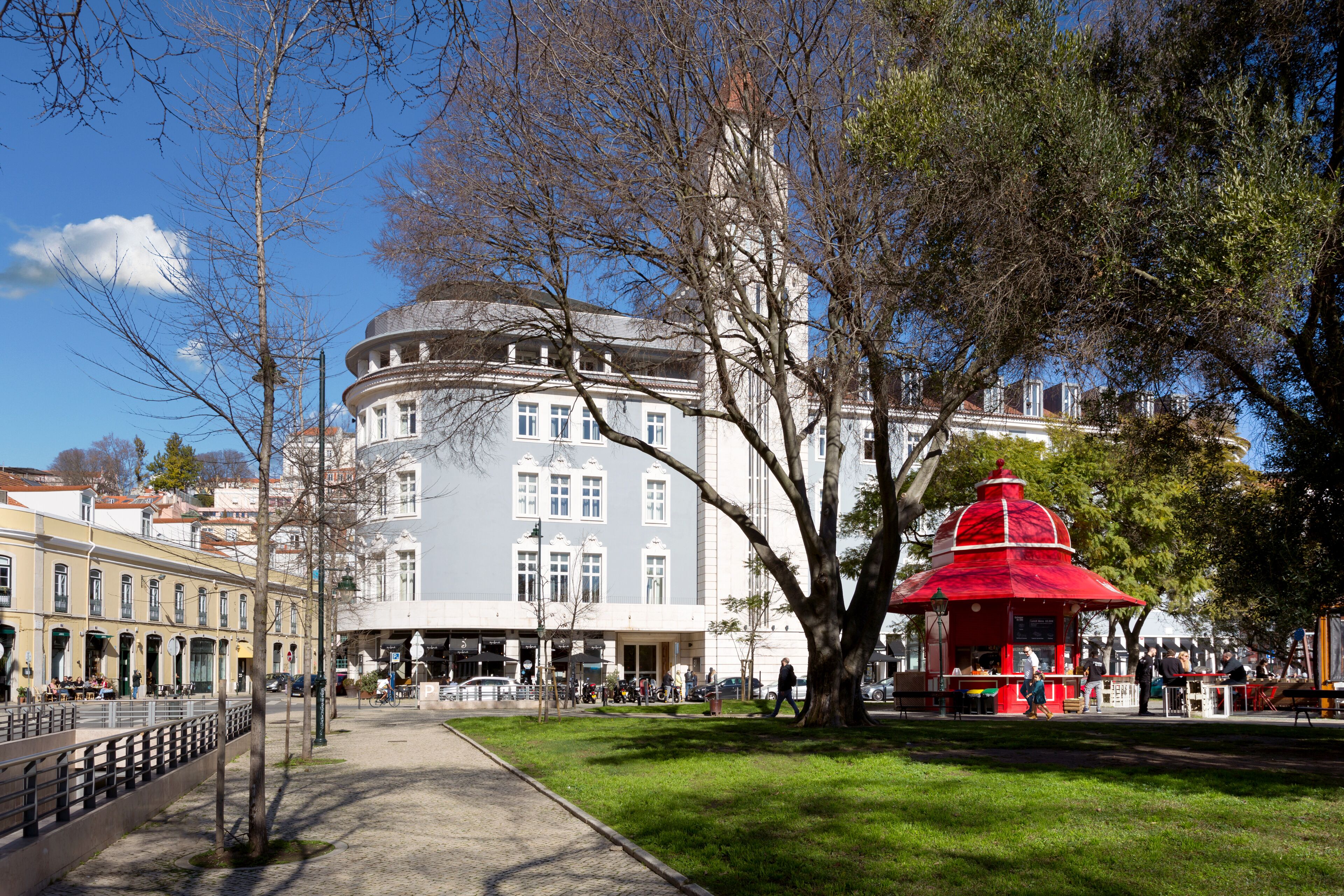 Ein historisches Gebäude mit abgerundeter Ecke, einem roten Pavillon und einem gepflasterten Weg.