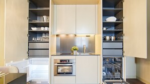 A compact kitchen with built-in appliances, including a refrigerator, oven, and dishwasher, and open shelving with dishes and cookware. - Lisbon Finestay 8 Building (Lisbon)