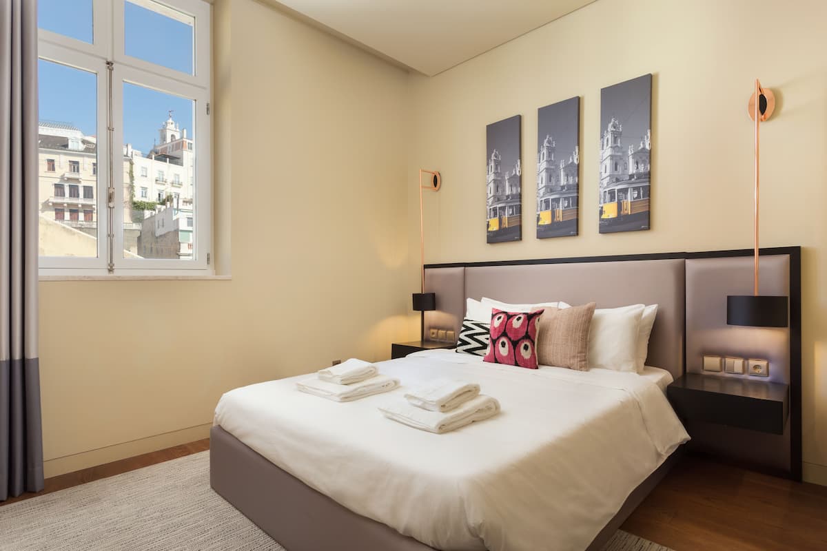 Ein Hotelzimmer mit einem großen Bett, einem Nachttisch mit Lampe und Blick auf Gebäude.