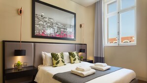 A neatly made bed with pillows, a bedside table with a lamp, and a framed cityscape picture on the wall. - Lisbon Finestay 8 Building (Lisbon)