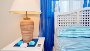 Una cama con cabecera blanca y ropa de cama azul a rayas, una mesita de noche con una lámpara, un pequeño florero decorativo y un control remoto.