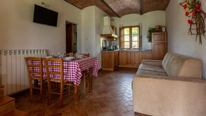 A dining area with a table set for four, wooden chairs, a sofa, and a kitchen in the background. - Apartment I Reucci Trilo5 (Pomarance)
