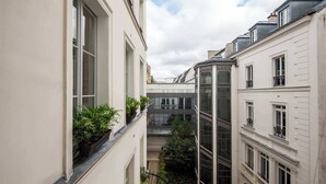 A narrow courtyard with buildings on either side, featuring balconies with potted plants and a glass elevator shaft. - My Opera de Paris II (Paris)