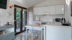 A modern kitchen with white cabinets, a central island, and a dining area with clear chairs.