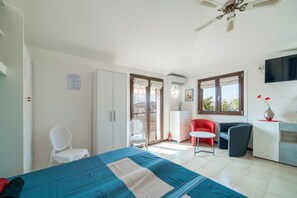 Quarto com cama, escrivaninha, cadeira, televisão e varanda com vista.