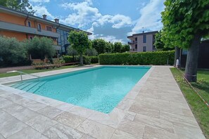 Ein rechteckiger Pool mit Fliesen umgeben, mit Grünflächen und modernen Gebäuden im Hintergrund.