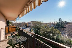 Uma varanda com mesa e cadeiras, com vista para uma área residencial com casas e árvores.