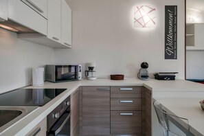 Eine moderne Küche mit integriertem Mikrowellenherd, Kaffeemaschine und Toaster. Es gibt einen Holzkasten mit Schubladen sowie einen Edelstahlbackofen.