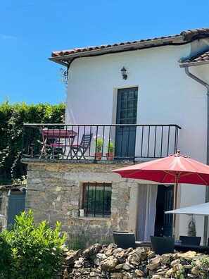A two-story building with a stone facade, a balcony with outdoor furniture, and a red umbrella. - Traditional French house with private pool and gardens. (Caylus)