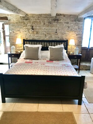 A bed with a floral bedspread, two bedside lamps, and a stone wall backdrop. - Traditional French house with private pool and gardens. (Caylus)