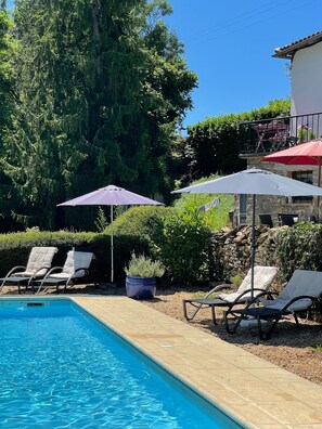 A swimming pool with lounge chairs and umbrellas, surrounded by greenery and a stone wall. - Traditional French house with private pool and gardens. (Caylus)