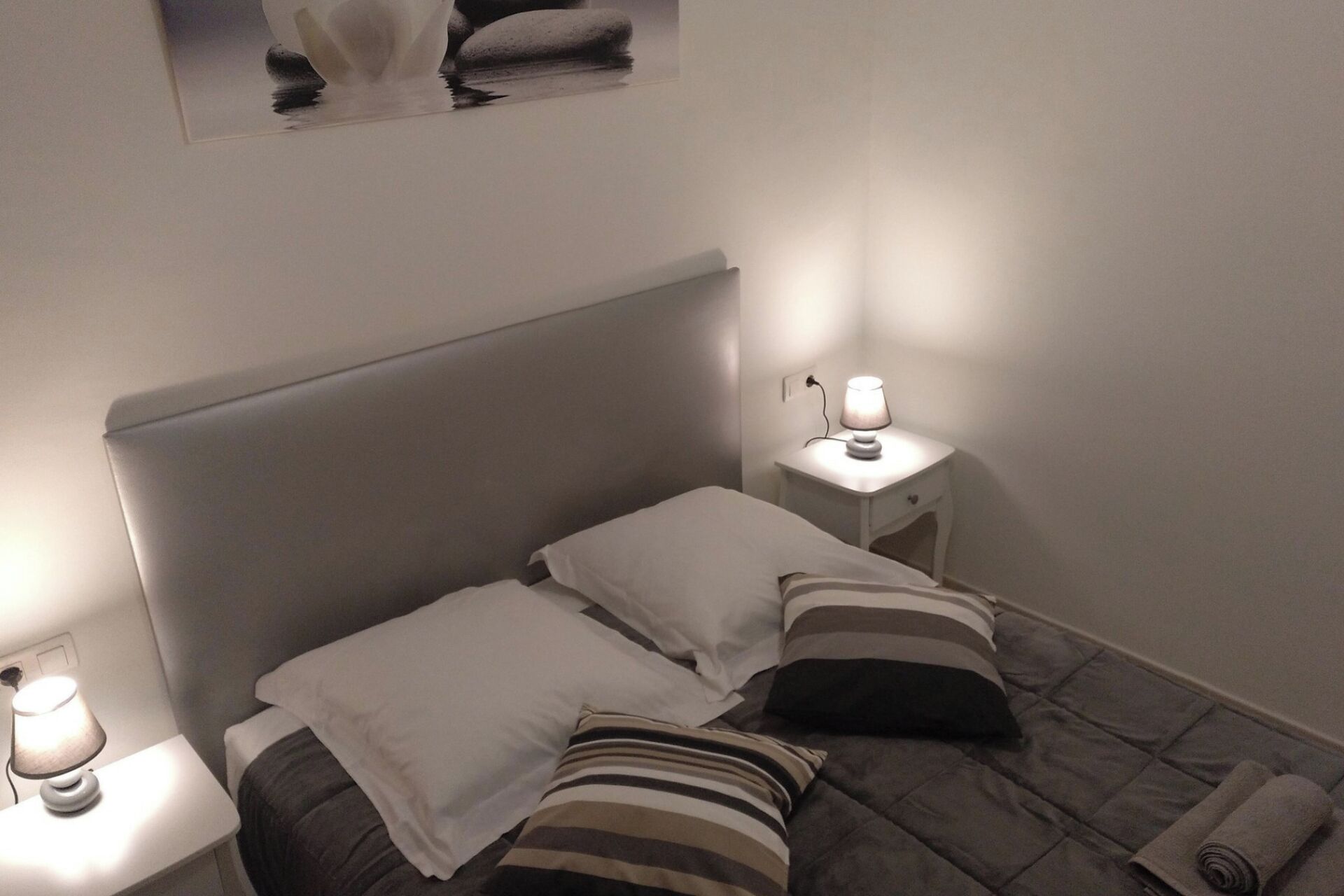 Ein kleines, ordentlich eingerichtetes Schlafzimmer mit einem Einzelbett, zwei Nachttischen und einem an der Wand hängenden Bild.