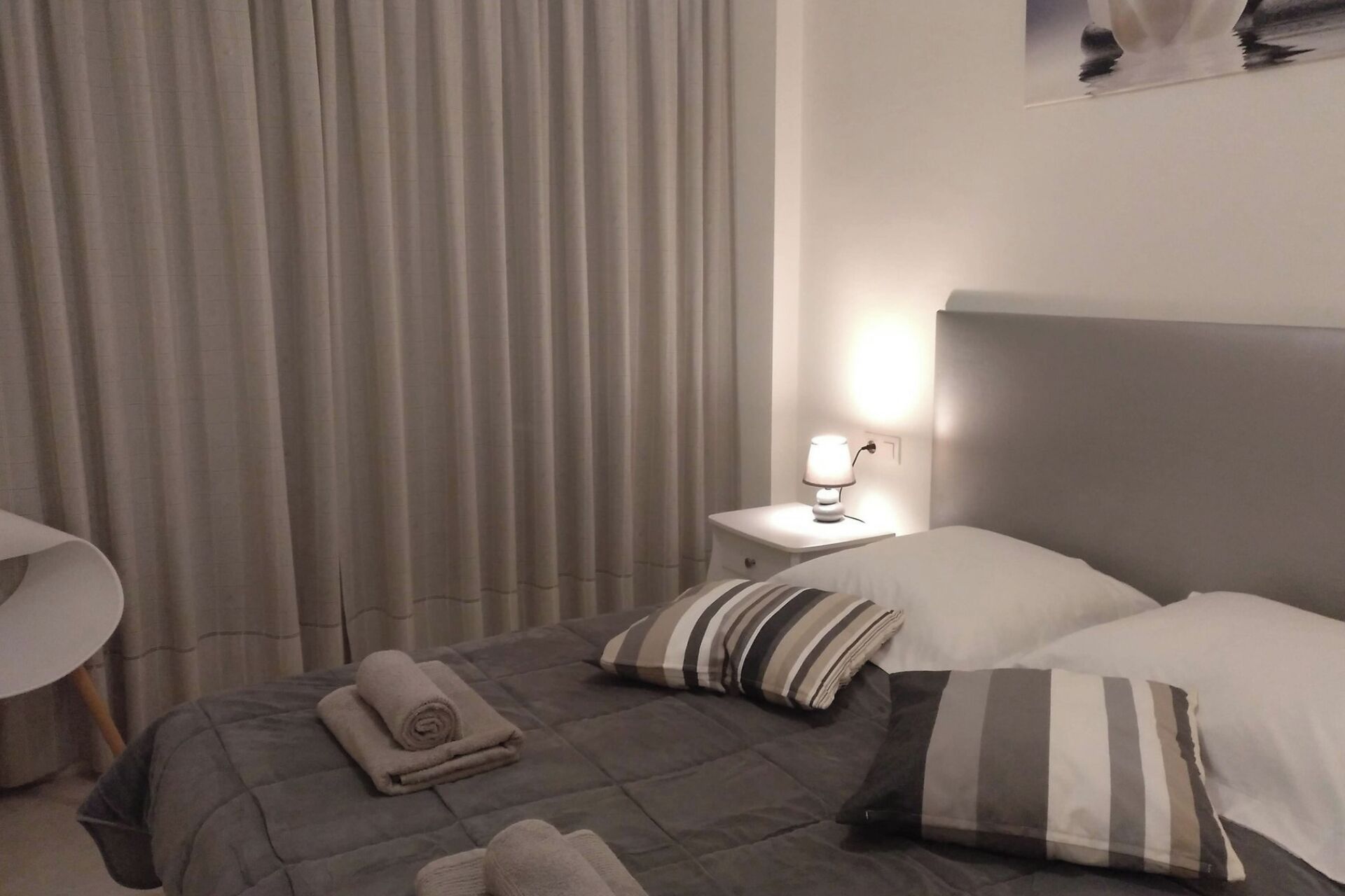 A hotel room with a bed, a bedside table with a lamp, and a curtain.