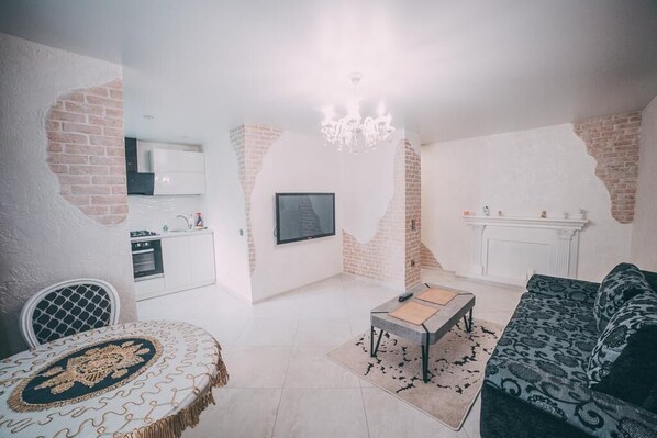 Ein Wohnzimmer mit einer Couch, einem Couchtisch und einem Essbereich mit Tisch und Stühlen. Im Hintergrund ist eine Küche erkennbar.