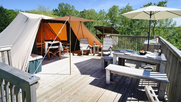 Een overdekt buitengebied met een houten terras, zitplaatsen en een eettafel.