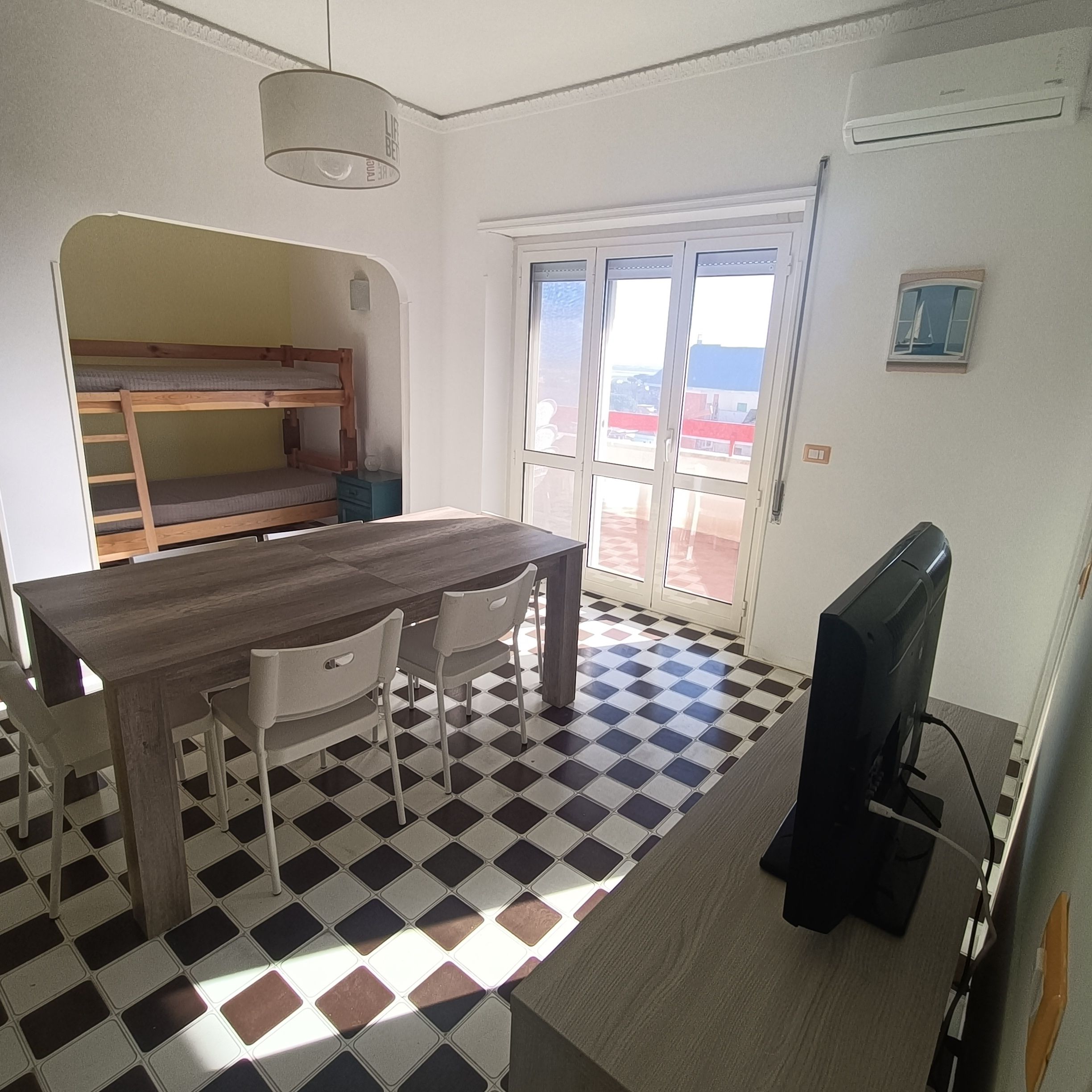 Une pièce avec une table en bois, deux chaises, un lit superposé, un téléviseur et un sol à carreaux.
