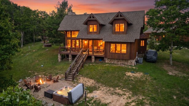 A two-story house with a deck, a hot tub, and a fire pit area.