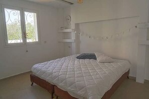 Ein Schlafzimmer mit einem Bett, einem Fenster und einem an der Wand befestigten Regal.