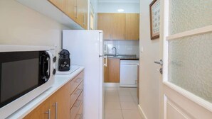 Una cocina compacta con armarios de madera, un refrigerador blanco, un microondas y una cafetera.