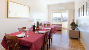 Un comedor con una mesa dispuesta para cuatro personas, un sofá y vistas a la ciudad a través de amplias ventanas.