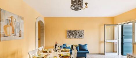 A dining area with a white table set for four, a blue sofa, and a modern chandelier.