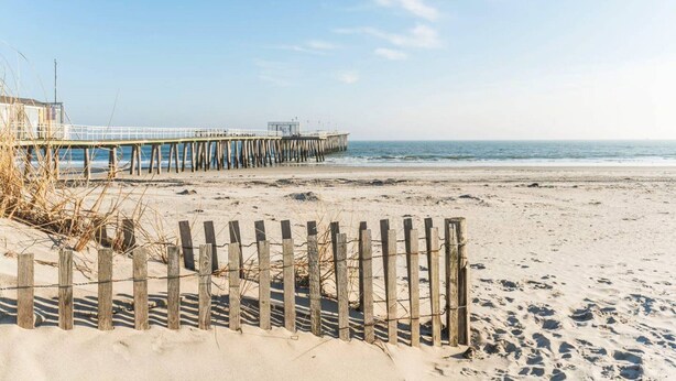 Una playa con un cerco de madera y un muelle que se adentra en el agua.
