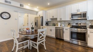 Una cocina moderna con armarios blancos, electrodomésticos de acero inoxidable y una mesa de comedor de madera con sillas.
