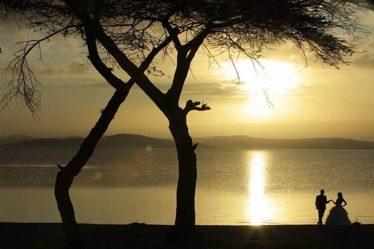 A silhouette of a couple holding hands against a sunset backdrop, with a calm lake and distant hills.