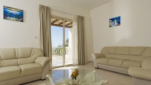 A living room with two beige sofas, a glass coffee table, and a balcony with curtains. - Luxury new villa on mountainside with private swimming pool & garden (Kathikas)