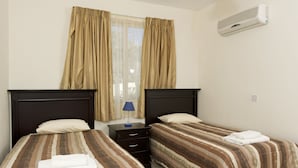 A twin room with two beds, a nightstand, an air conditioner, and a window with curtains. - Luxury new villa on mountainside with private swimming pool & garden (Kathikas)