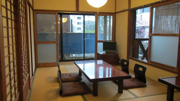 A traditional Japanese room with tatami flooring, a low table with cushions, a television, and sliding doors leading to a balcony.