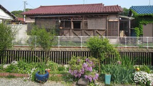 A traditional wooden house with a tiled roof, surrounded by a garden with various plants and flowers.