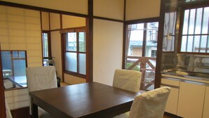 A dining area with a wooden table and striped chairs, a view of the outside through large windows, and a kitchen area with a stove.