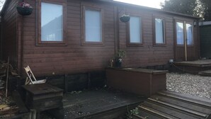 Una cabaña de madera con cuatro ventanas, un porche pequeño y una chimenea.