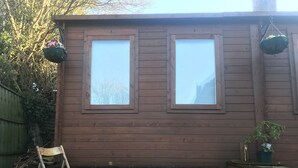 Un cobertizo de madera con dos ventanas, una escalera y una planta en maceta.