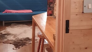 Interior de una cabaña de madera con un banco de madera, una cortina azul y una pequeña mesa con un objeto decorativo.