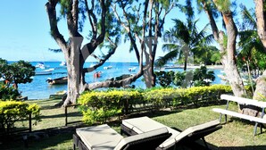 A beach view with lounge chairs, trees, and boats in the water.