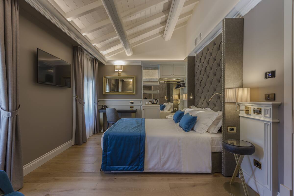 A hotel room with a bed, a desk, a mirror, and a TV.