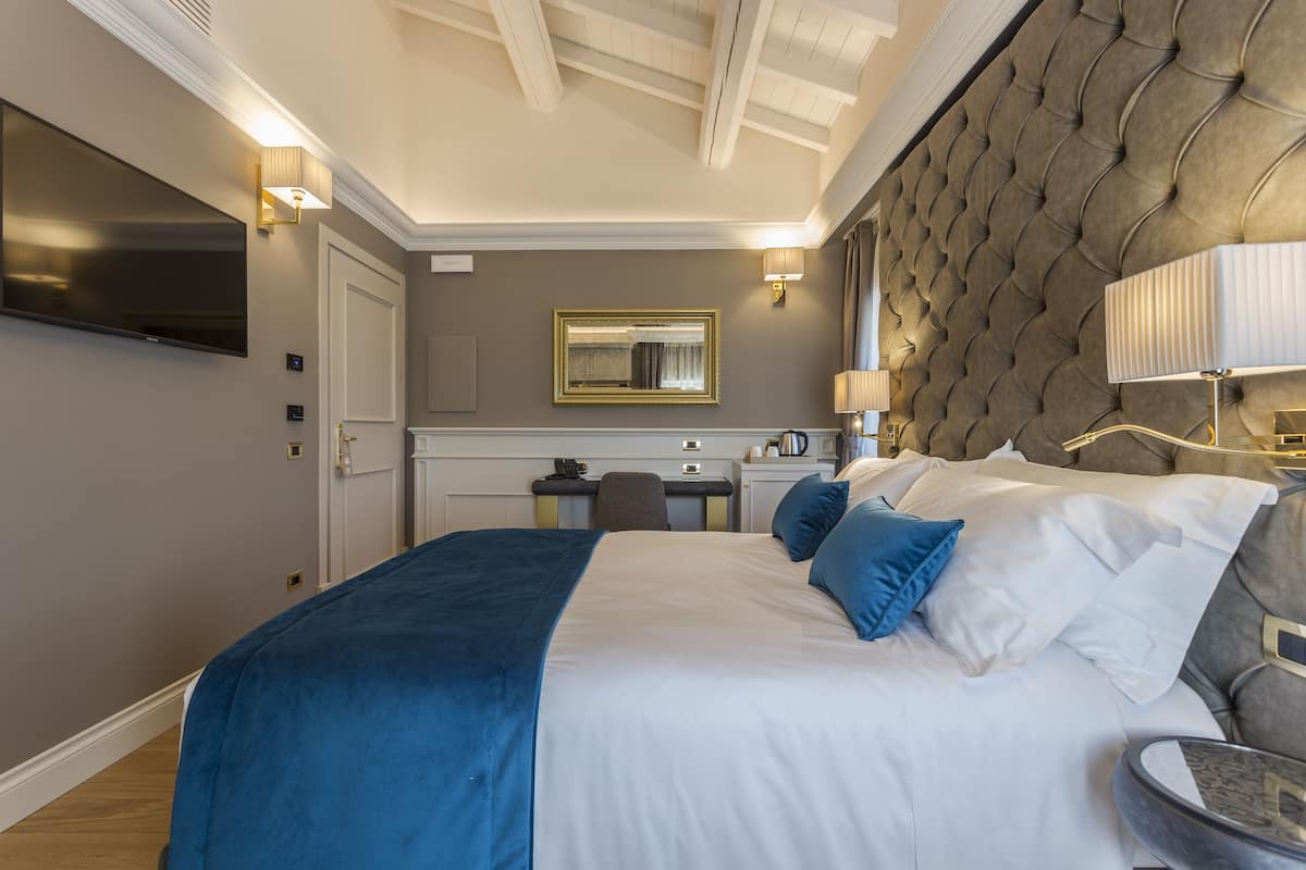 A modern hotel room with a large bed, a flat-screen TV, a desk with a chair, and a comfortable seating area.