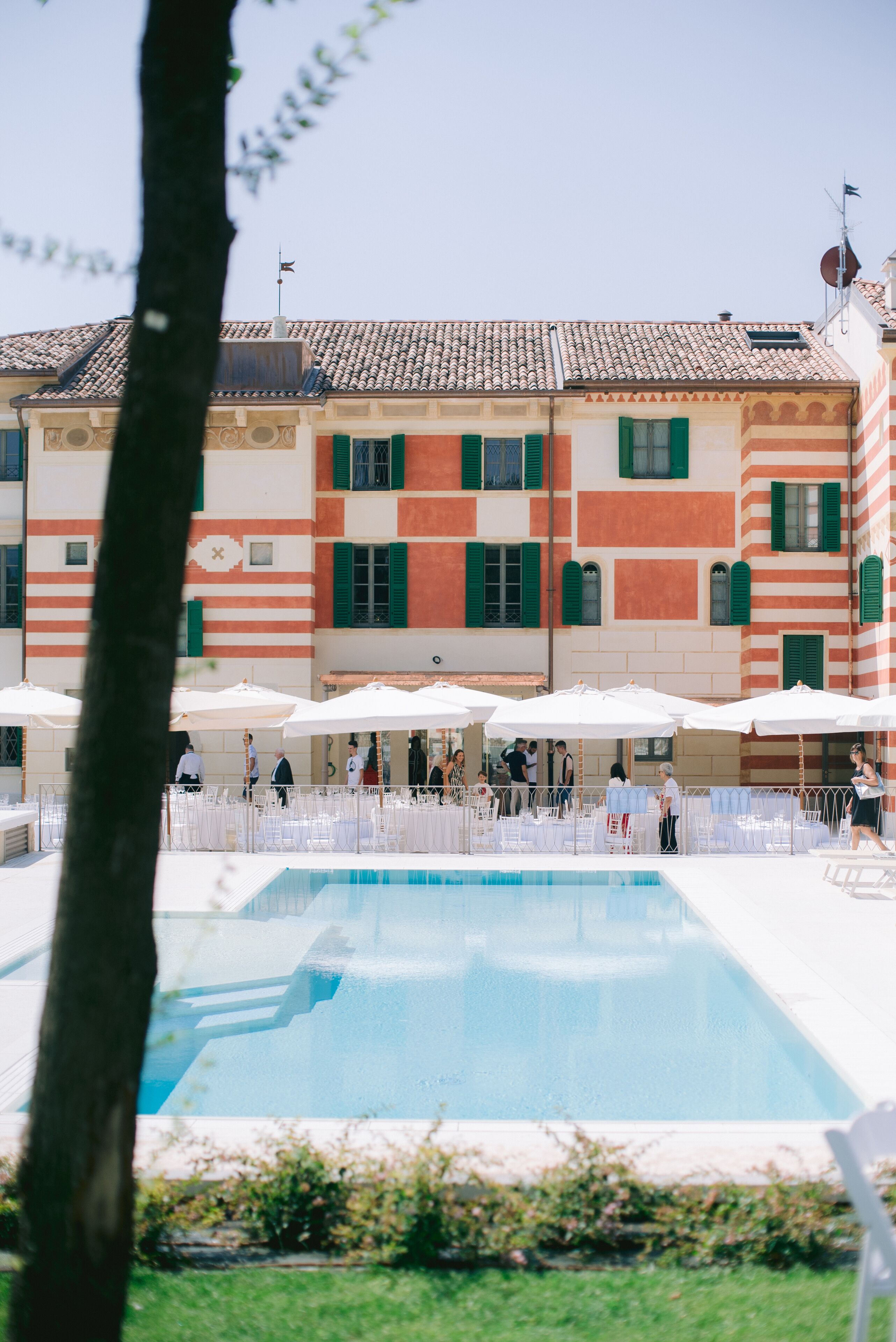 A poolside area with outdoor seating and a building with striped facade and green shutters.