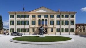 A large, classical building with a symmetrical facade, green shutters, and a central statue.