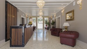 A reception area with a reception desk, a chandelier, a mirror, and a seating area with a sofa and ottoman.